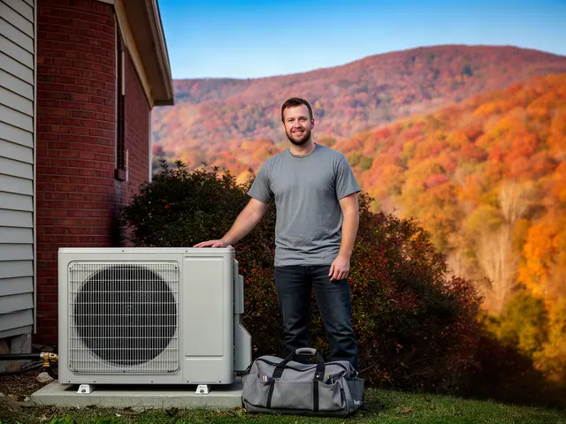 An HVAC contractor beside a new outdoor unit at a brick house with autumn ridges beyond.